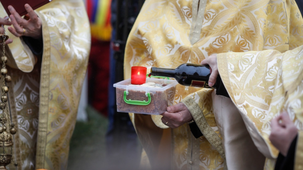 Popă ortodox care toarnă vin pe o mâncare funerară în timpul unei ceremonii.