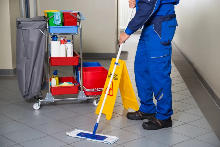 Ștergerea podelei în toaletă O femeie de serviciu șterge plăcile de pe podea în holul care duce la toaletă.