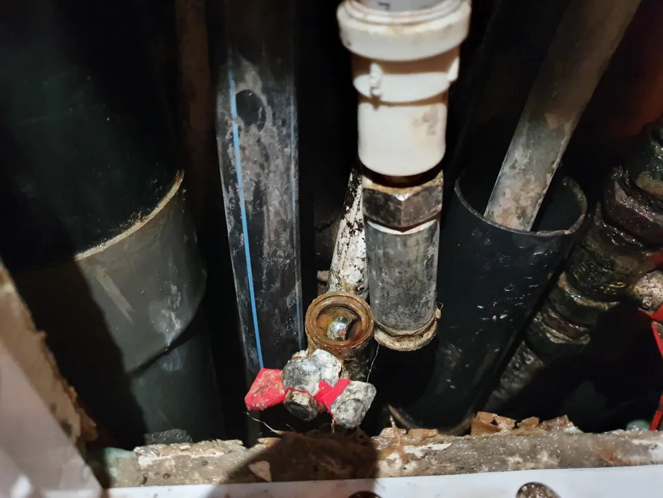 Corroded water pipe connections with rust and mineral buildup in a confined space.