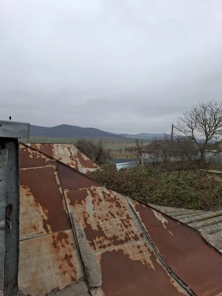Rusty metal roof overlooking rural landscape (41547) A rusty sheet metal roof with visible corrosion set against a rural backdrop under a cloudy sky.