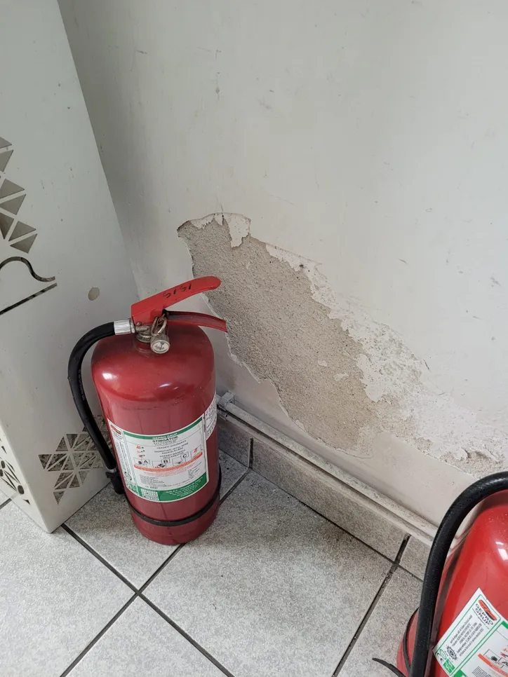 Peeling wall paint near fire extinguisher (29959) Peeling paint on wall with fire extinguisher nearby, highlighting moisture damage.