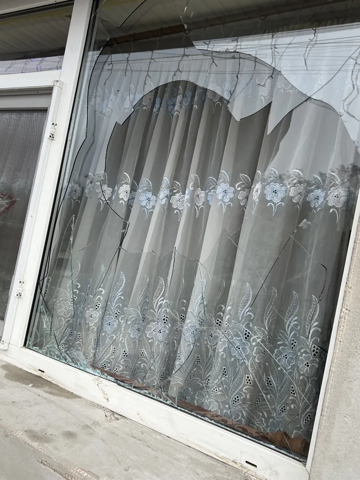 Cracked window with decorative curtains (40241) A window with significant cracks is behind lace-patterned curtains, indicating damage.