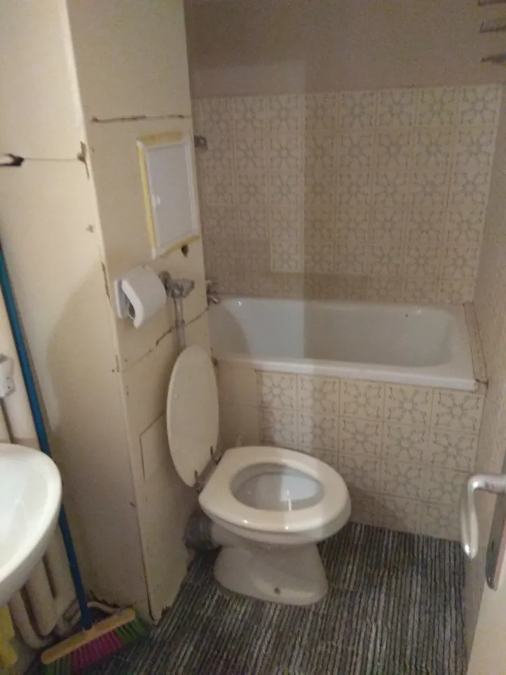 Baie compactă cu toaletă plasată necorespunzător (18824) Baie mică cu toaletă plasată necorespunzător, care este așezată lângă cadă, evidențiind problemele de utilizare a spațiului.