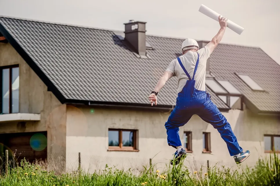 Constructorul fericit Un constructor fericit sărind în fața casei cu planurile în mână.
